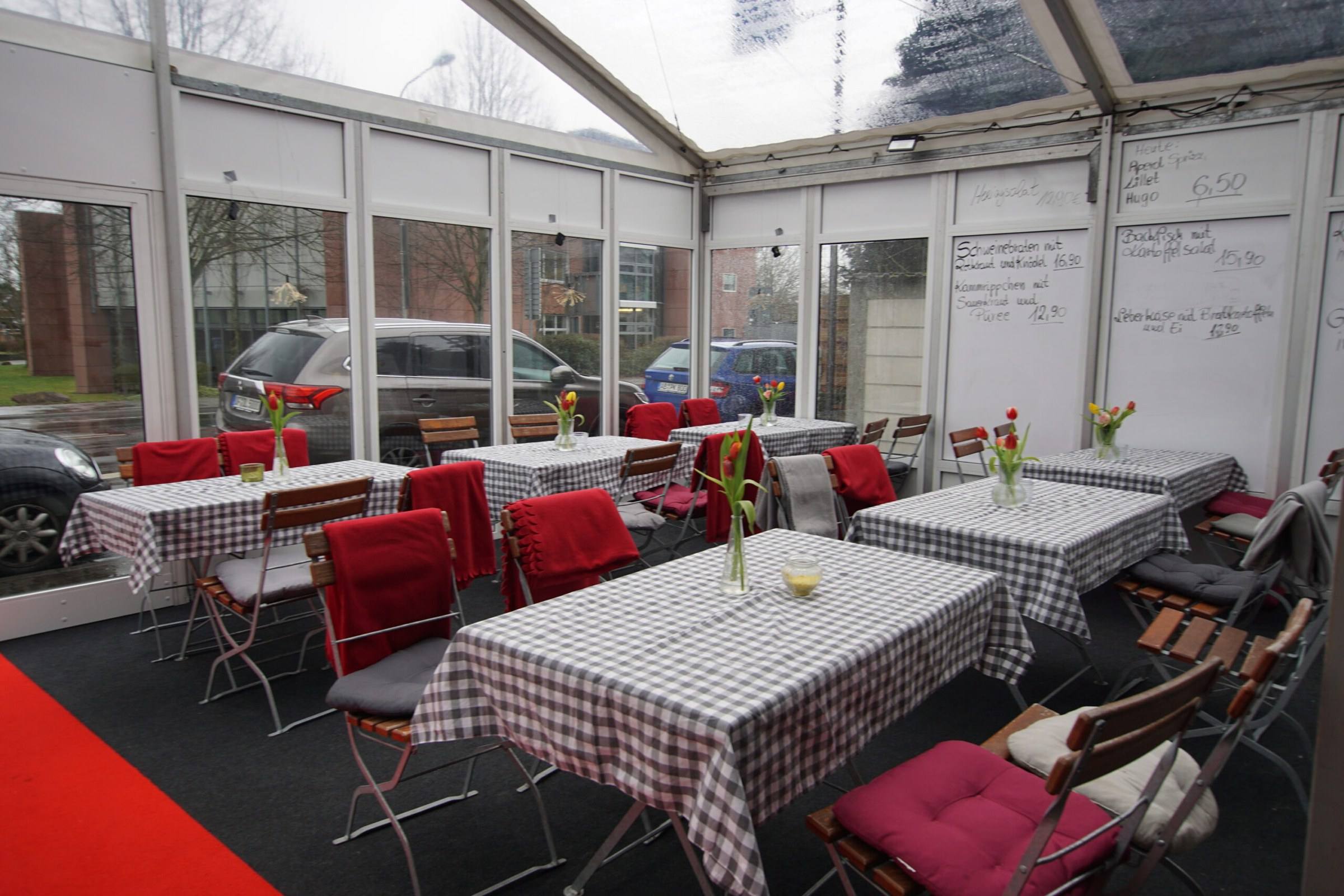 Überdachter Wintergarten mit karierten Tischdecken und roten Polstern
